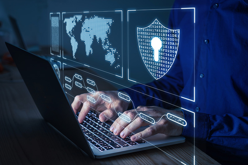 A person types on a laptop, surrounded by digital graphics like a world map and a shield symbolizing cybersecurity, illustrating modern policing and data protection strategies.